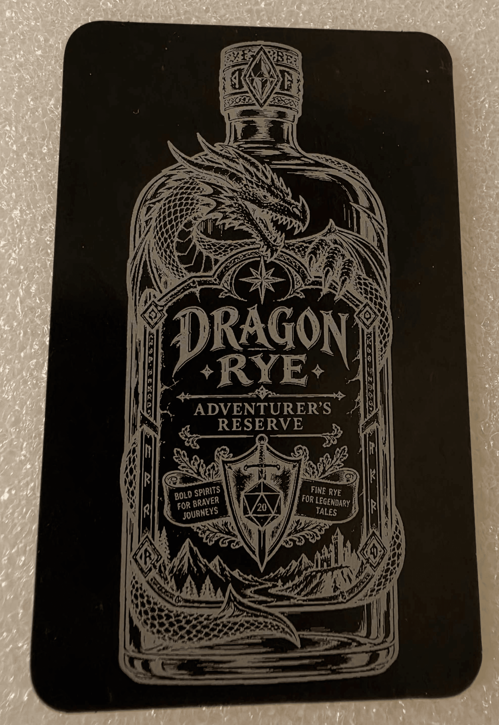 Black engraved metal card featuring an ornate dragon-themed bottle design